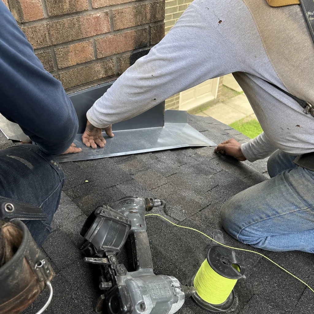 Roofers installing metal chimney flashing on shingled roof